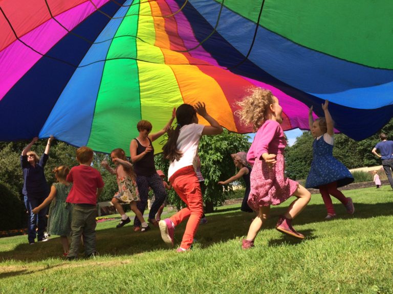 Children running under a rainbow coloured parachute