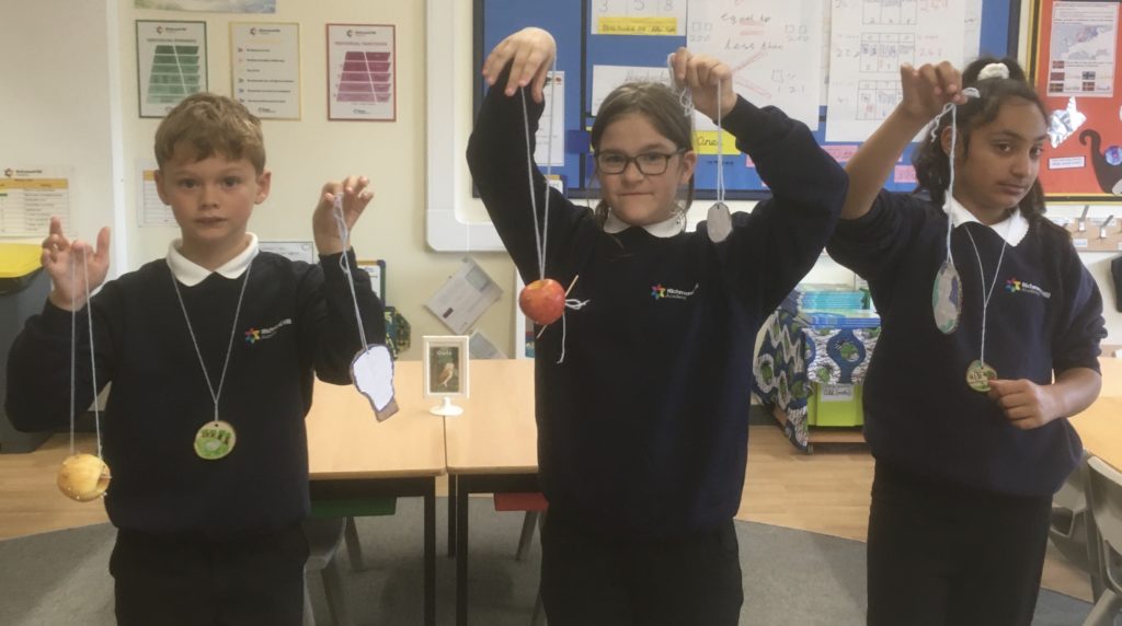 3 children who are green influencers in school uniform holding up apple feeders 