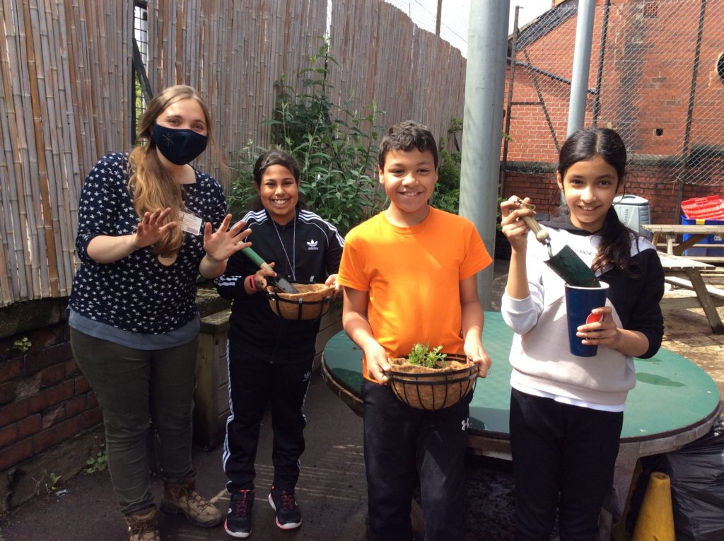 Green mentor Elaine Brown wearing a mask and standing outside with 3 children who are holding pots and gardening equipment