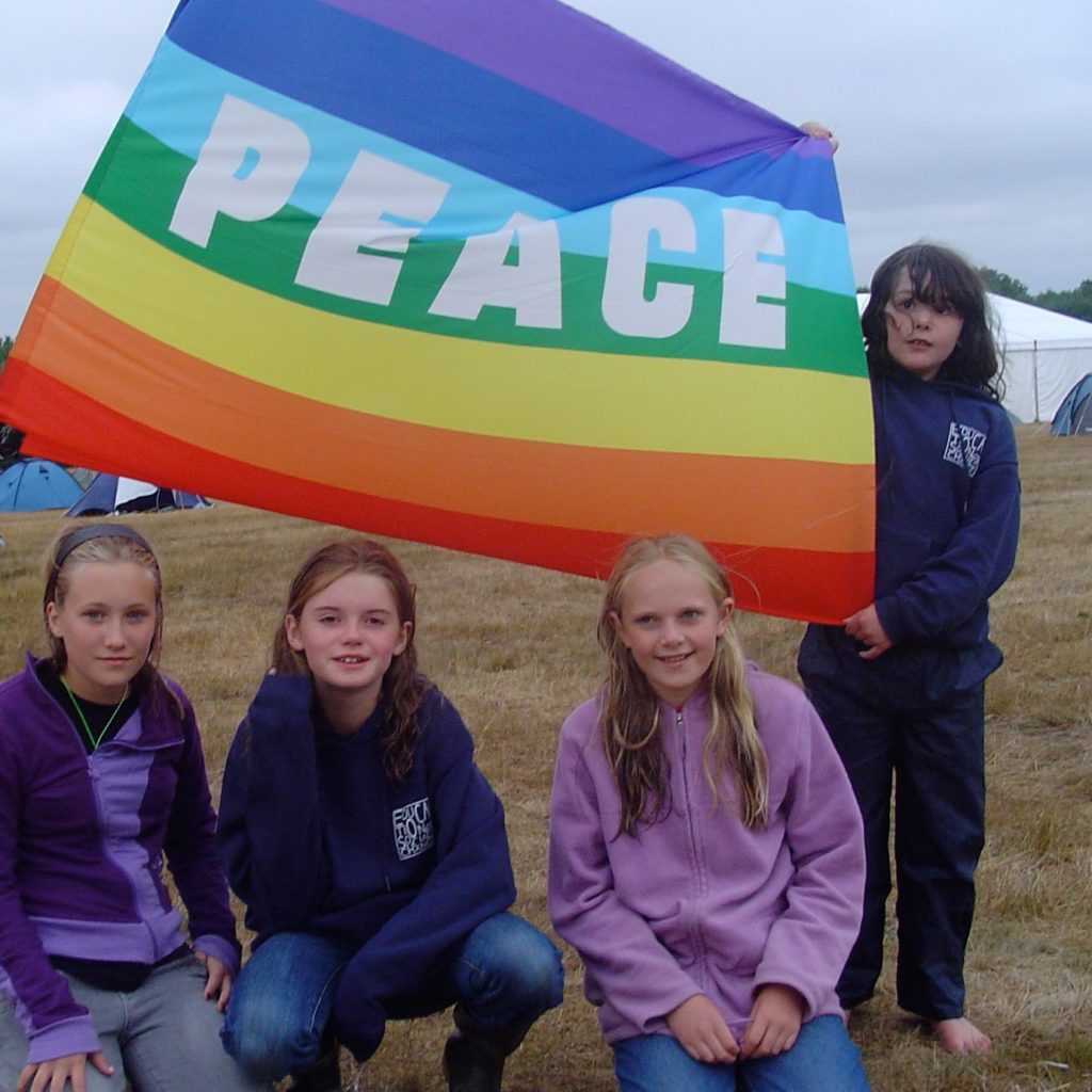 A group of 10-12 year olds at camp, holding a rainbow flag bearing the motto 'PEACE'