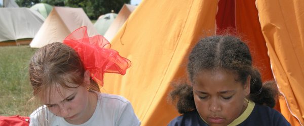 two children making friendship bands in front of a tent