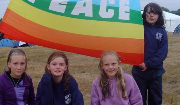 A group of 10-12 year olds at camp, holding a rainbow flag bearing the motto 'PEACE'